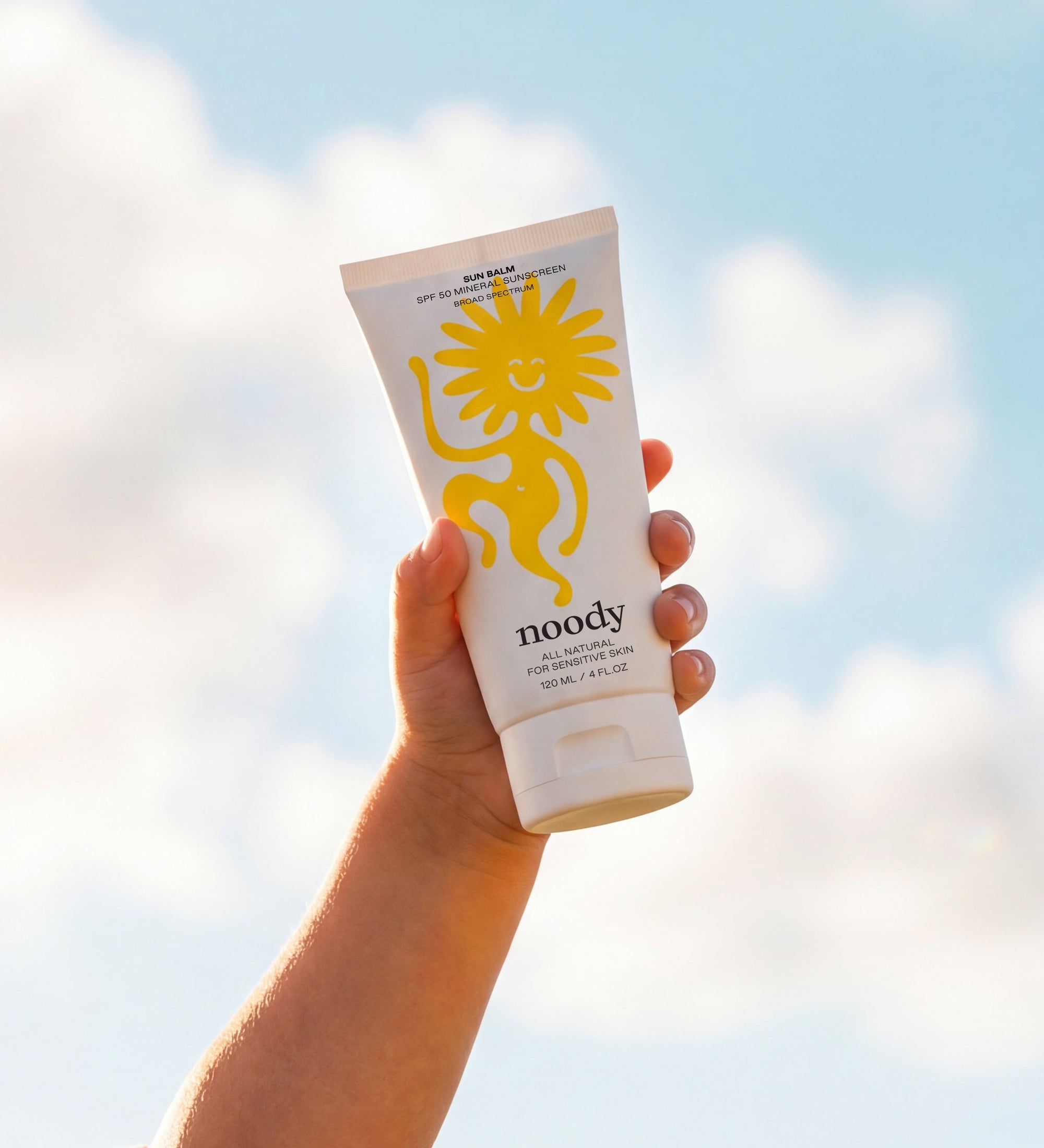 Hand holding a sunscreen tube with a blue sky and clouds in the background
