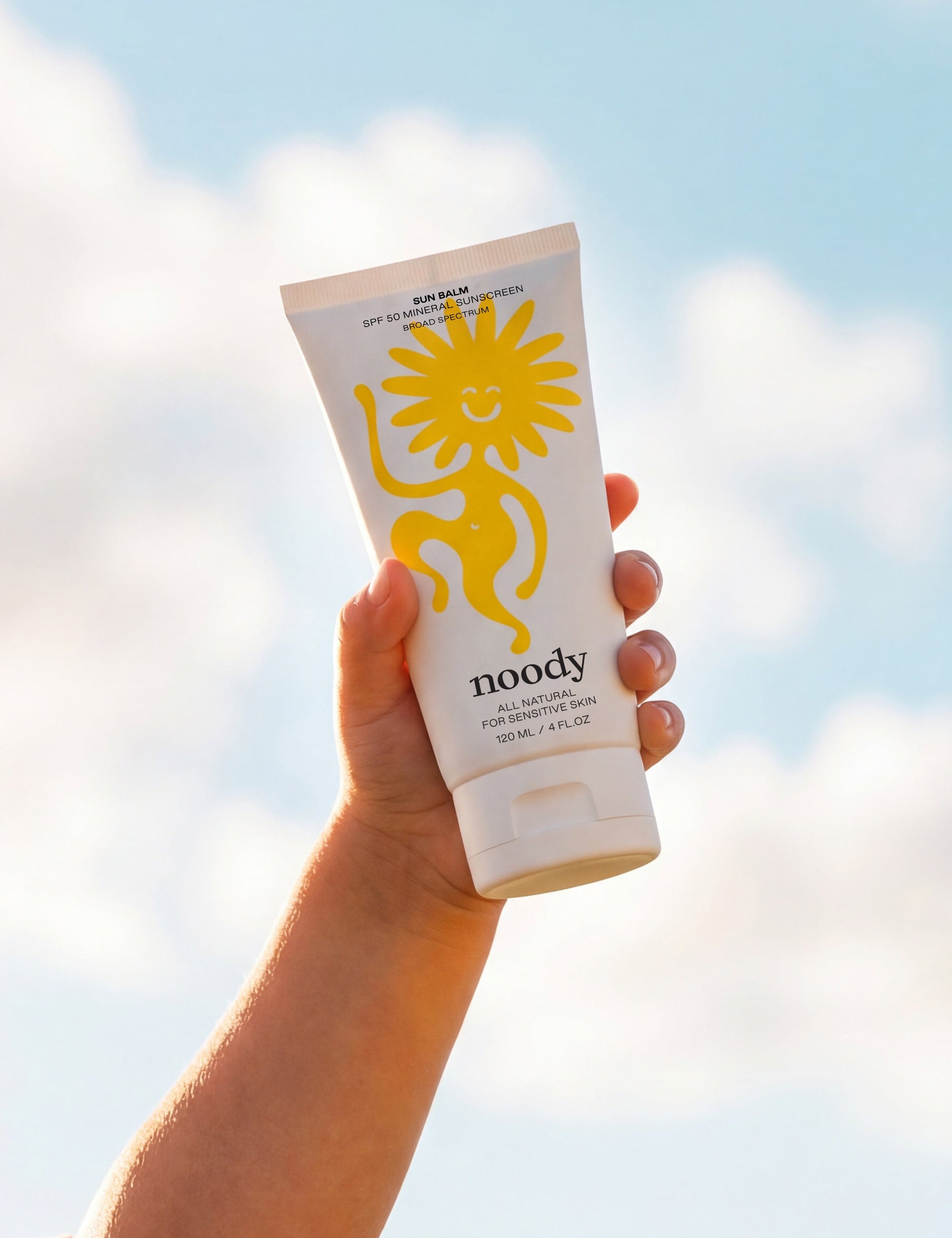 Hand holding a sunscreen tube with a blue sky and clouds in the background