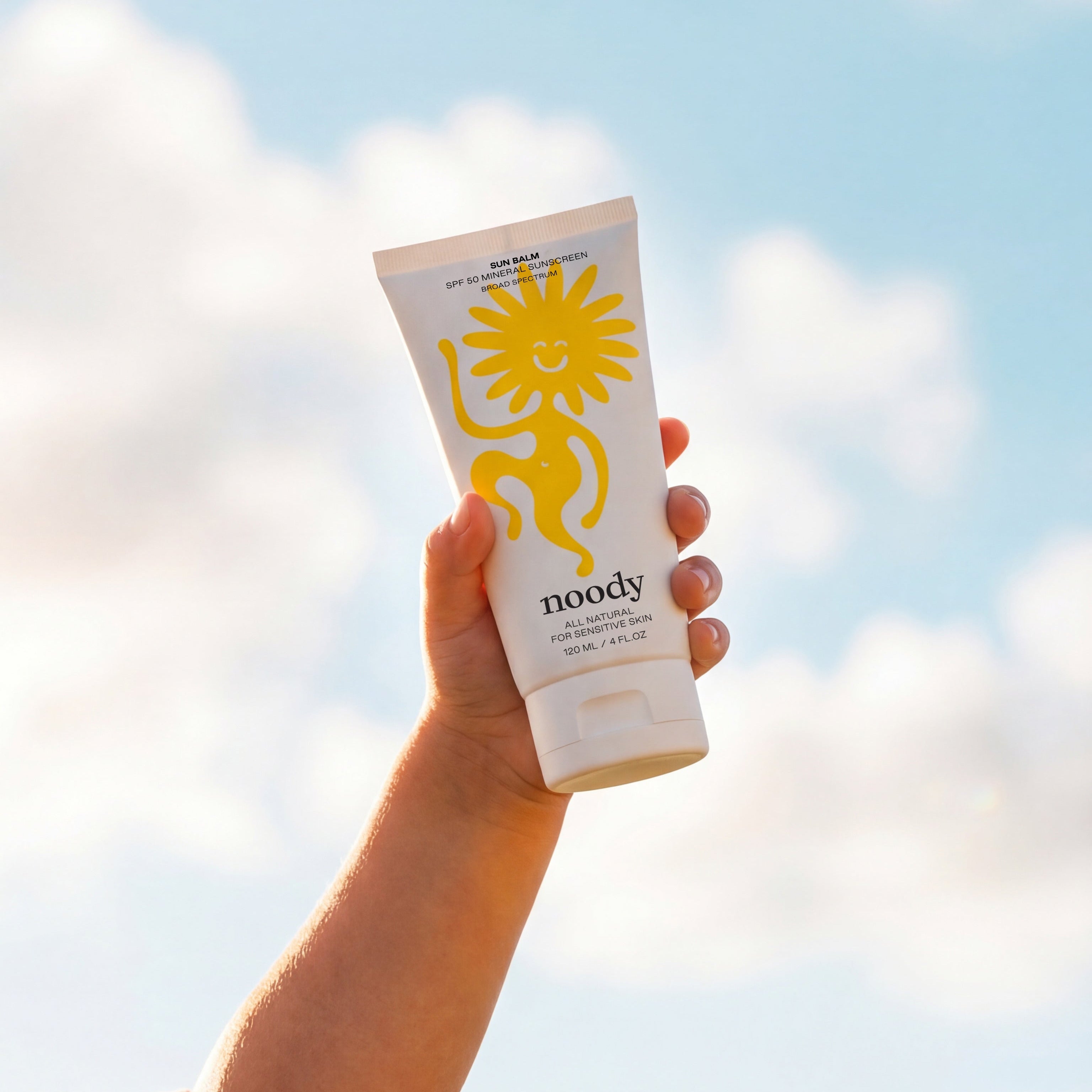 Hand holding a sunscreen tube with a blue sky and clouds in the background
